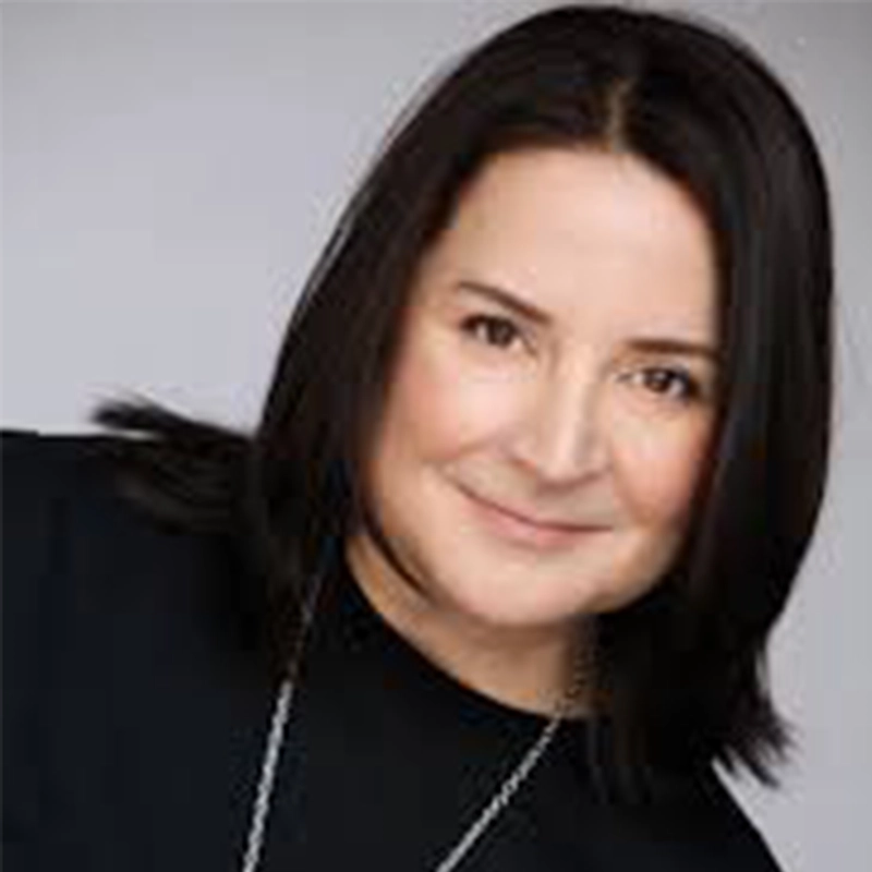 Sandra Valls, with straight, shoulder-length dark brown hair, wears a black top and a necklace as she smiles gently at the camera against a plain light gray background. Her head is slightly tilted, giving her a natural, friendly expression.