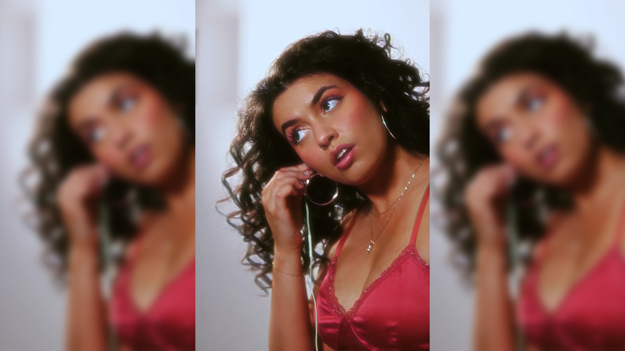 A woman with curly hair wears a pink camisole and gold jewelry, adjusting a large hoop earring. Her makeup is bold, with pink eyeshadow and lipstick. The background is blurred, with the image mirrored on both sides for a dreamy effect—a signature portrait style often seen in Sara Al-Bazali’s striking “Wait For It” series.
