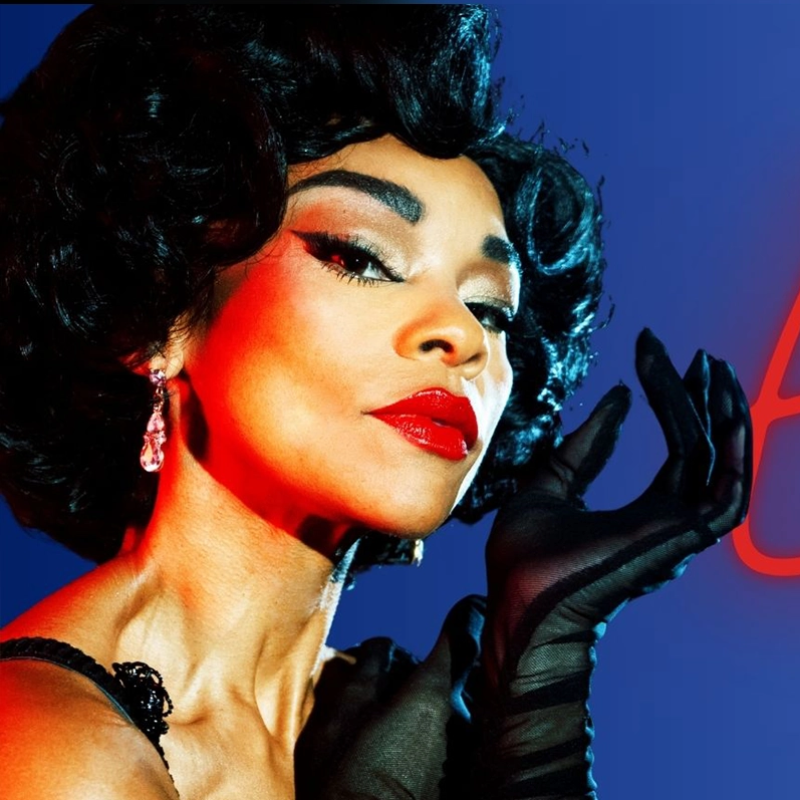 A glamorous woman with short, wavy black hair and red lipstick wears elegant earrings and sheer black gloves. She poses confidently against a blue background with dramatic red lighting highlighting her face and hand, exuding vintage Hollywood style.