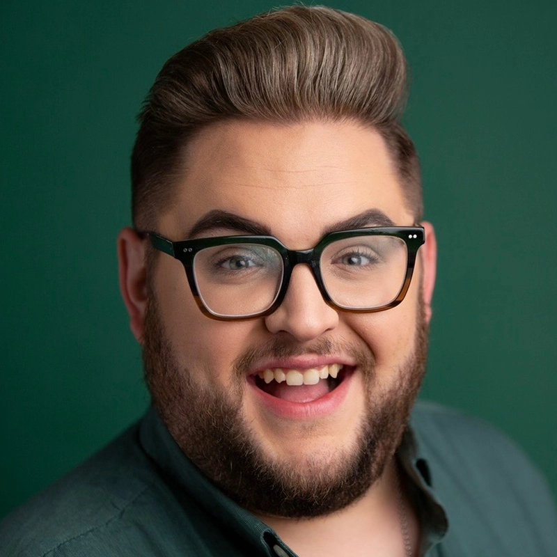 A smiling man with light skin, styled brown hair, a trimmed beard, and mustache wears black-framed glasses and a dark green shirt. Joshua Harris is pictured against a plain dark green background.