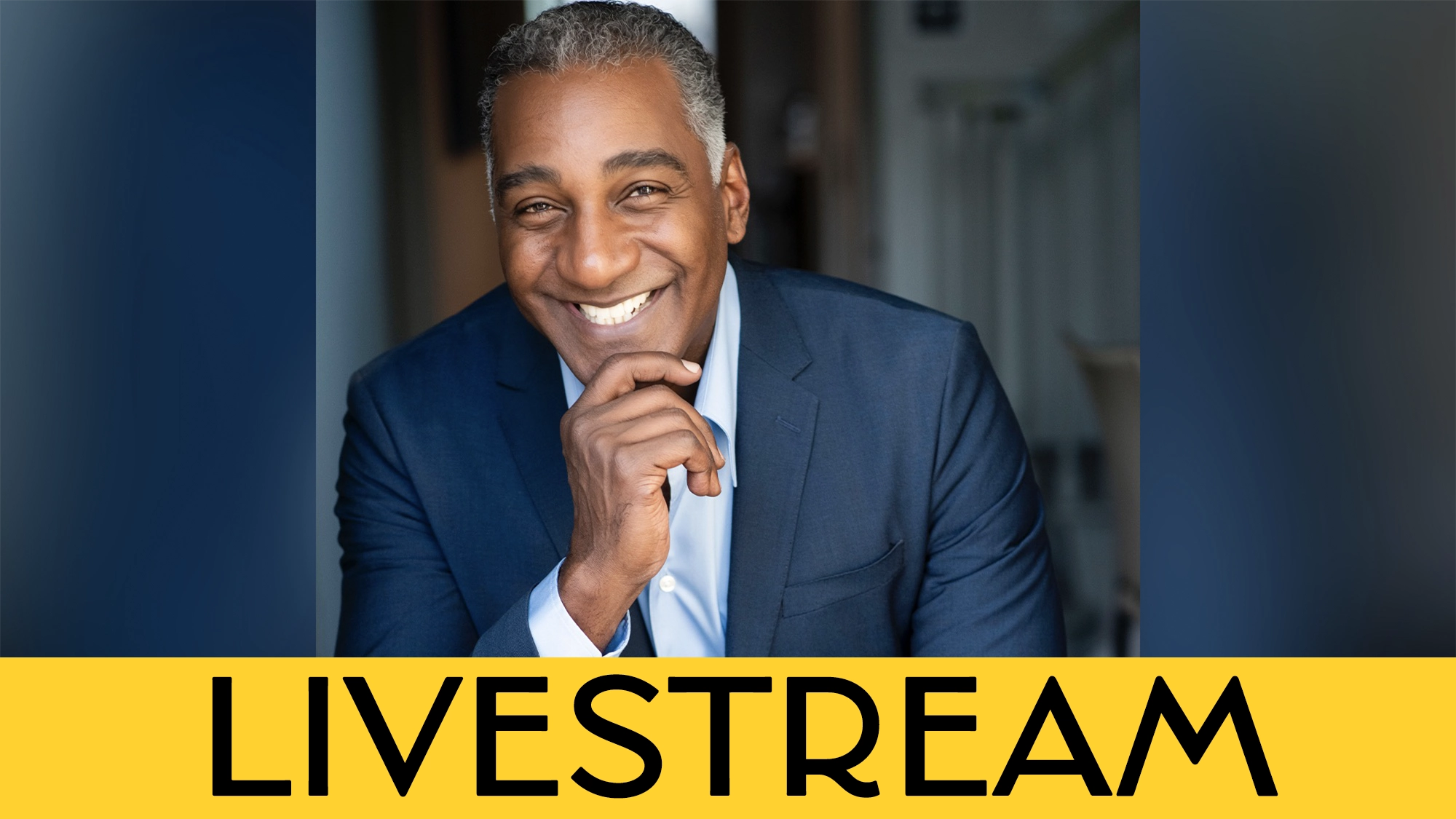 A smiling man in a blue suit poses with his hand on his chin. He has short gray hair and is in a brightly lit hallway, bringing Broadway charm to the scene. The word “LIVESTREAM” appears boldly on a yellow banner across the bottom.