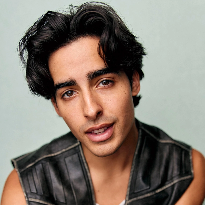 Joseph Torres, a young man with wavy dark hair and prominent eyebrows, looks into the camera. He has light brown skin, brown eyes, and wears a sleeveless black leather vest over a white shirt against a neutral light background.