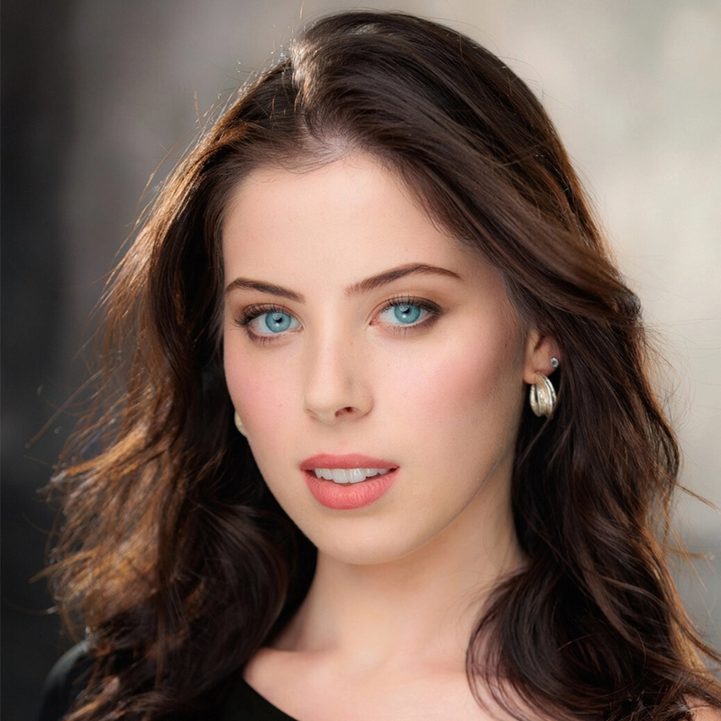A young woman with wavy brown hair and striking blue eyes gazes at the camera. She wears silver hoop earrings and a black top. The background is softly blurred, drawing focus to her clear skin and natural makeup.