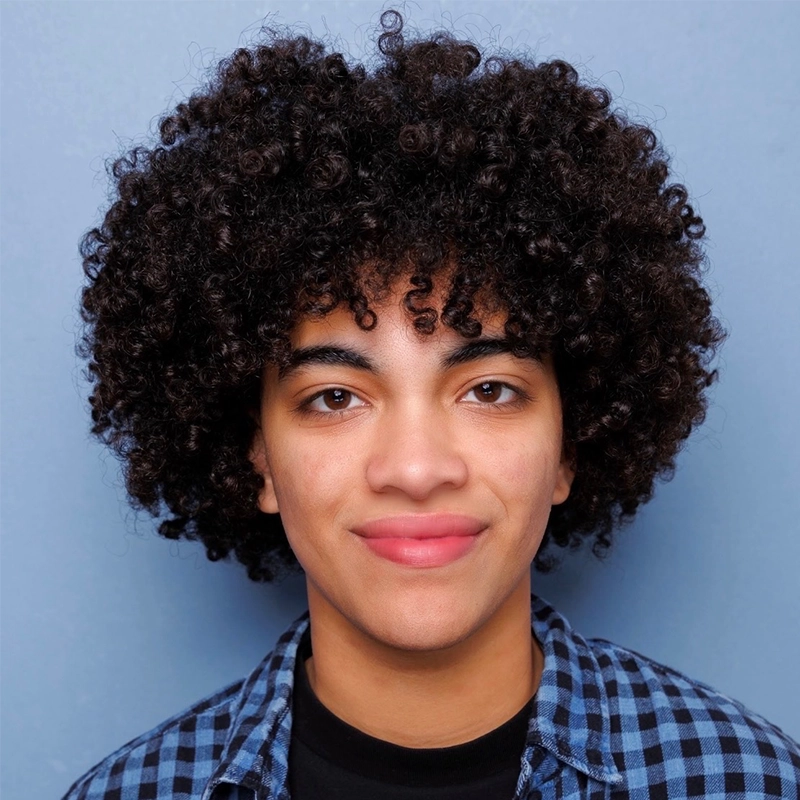 A young person with medium skin, short curly dark hair, and a friendly smile stands in front of a plain blue background, wearing a blue and black checkered shirt over a black t-shirt. This image features Gaël Mouton-Sady.