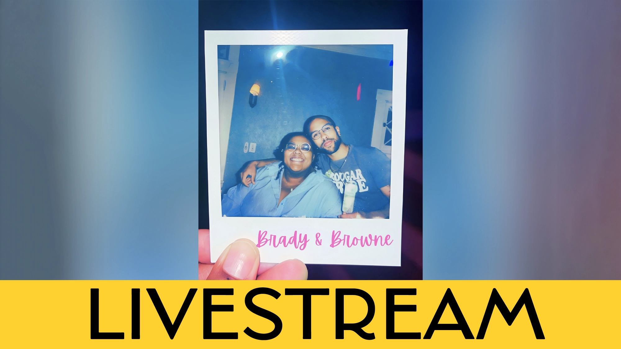 A hand holds a polaroid photo of two people smiling, one with glasses and one with a beard. 