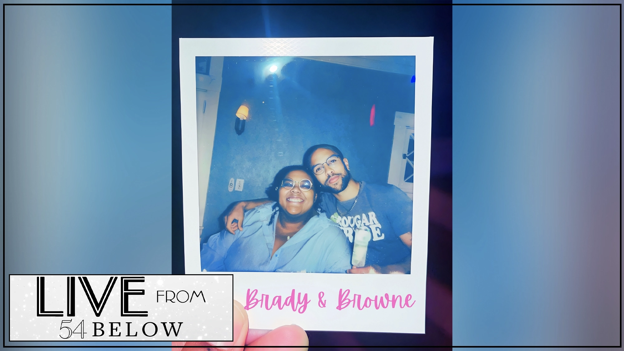 LIVE Flame Show Art A hand holds a Polaroid of two smiling people sitting close together; one wears glasses and a blue shirt, the other has a beard and gray shirt. The words “Brady & Browne” are written in pink, hinting at the musical duo of Amara Janae Brady and Xander Browne. The bottom left reads “LIVE FROM 54 BELOW” in bold black text.