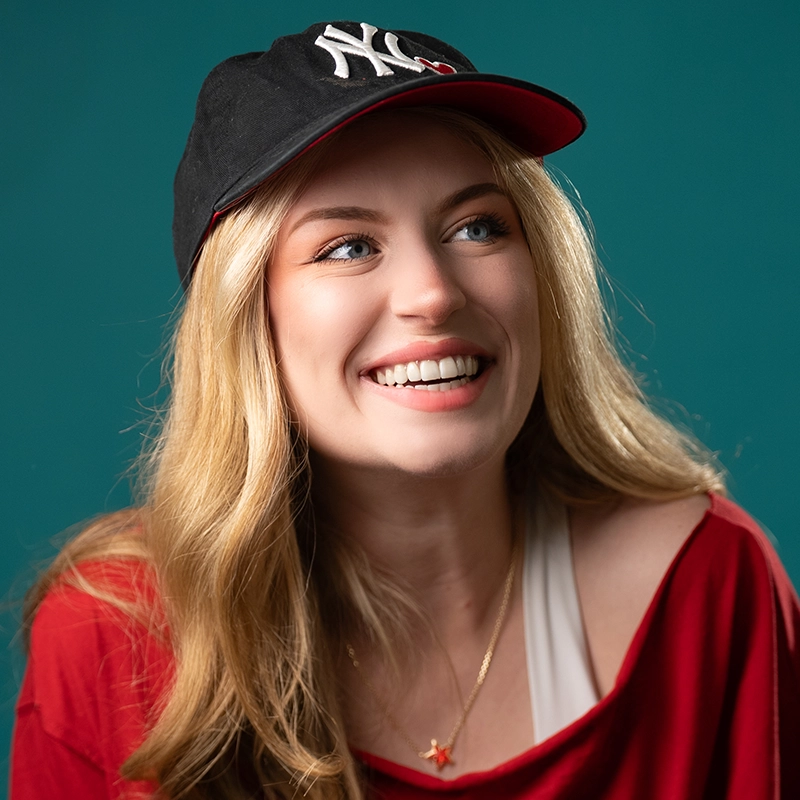 A smiling young woman with long blonde hair wears a black 