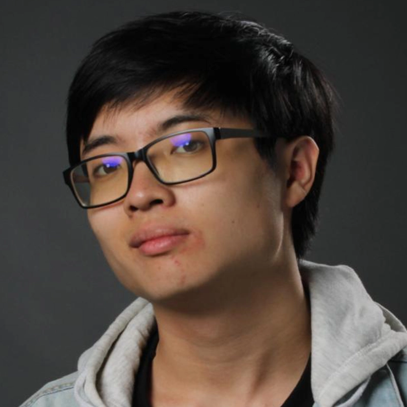 A young person with short black hair and glasses looks at the camera with a neutral expression. Casey Keeler wears a light denim jacket over a gray hoodie. The background is solid and dark.