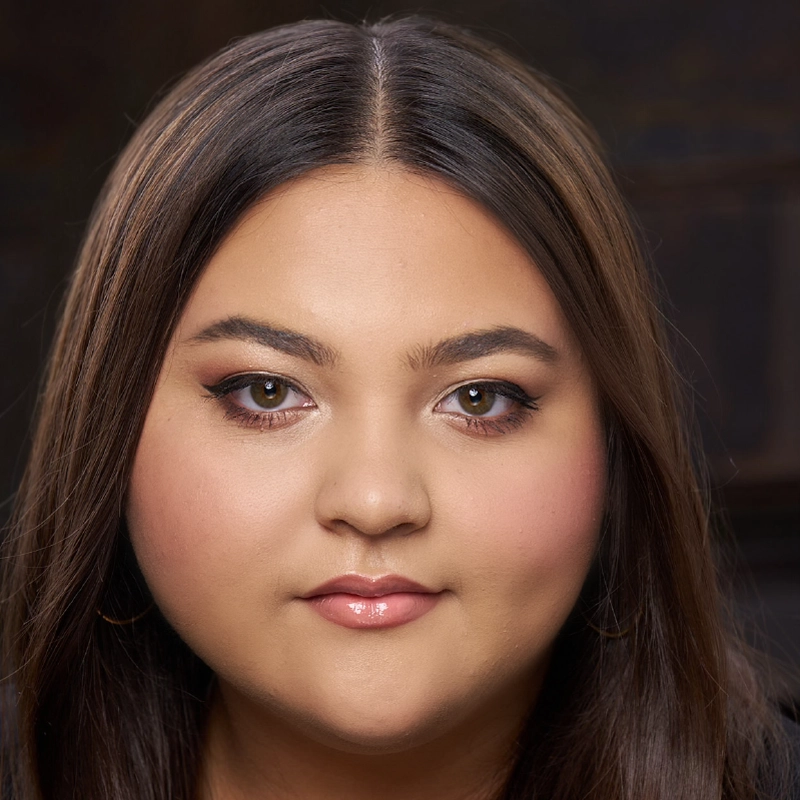 A young woman with straight dark brown hair, parted in the middle, and fair skin. She has brown eyes, subtle eyeliner, soft pink blush, glossy nude lips, and gold hoop earrings. The mood and depth of the portrait are reminiscent of a style favored by Salvador Diaz-DeBose; the background is dark and blurred.