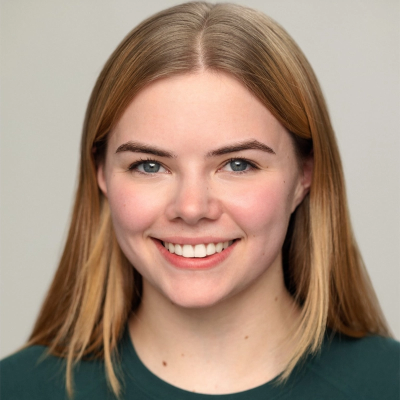 A young woman, Addie Green Peterson, with straight, shoulder-length blonde hair smiles warmly. She has fair skin, blue eyes, and natural makeup. She wears a dark green top and is posed against a simple, light grey background.