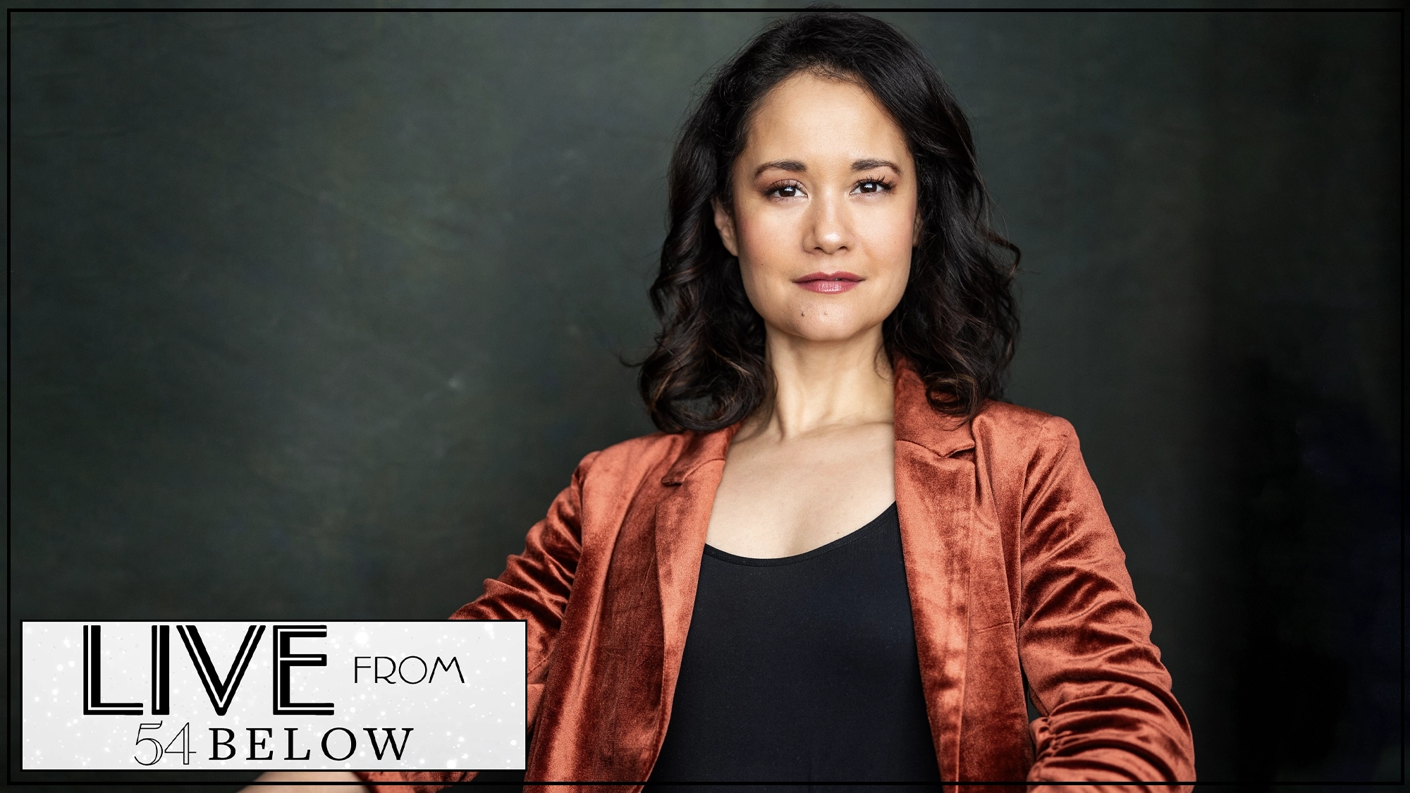 A confident woman with wavy dark hair wears a burnt orange velvet blazer over a black top, standing against a dark green background. Bottom left features a white box with black text: “LIVE FROM 54 BELOW.” Experience the magic of “When You Wish Upon A Star” in this exclusive livestream performance by Ali Ewoldt.