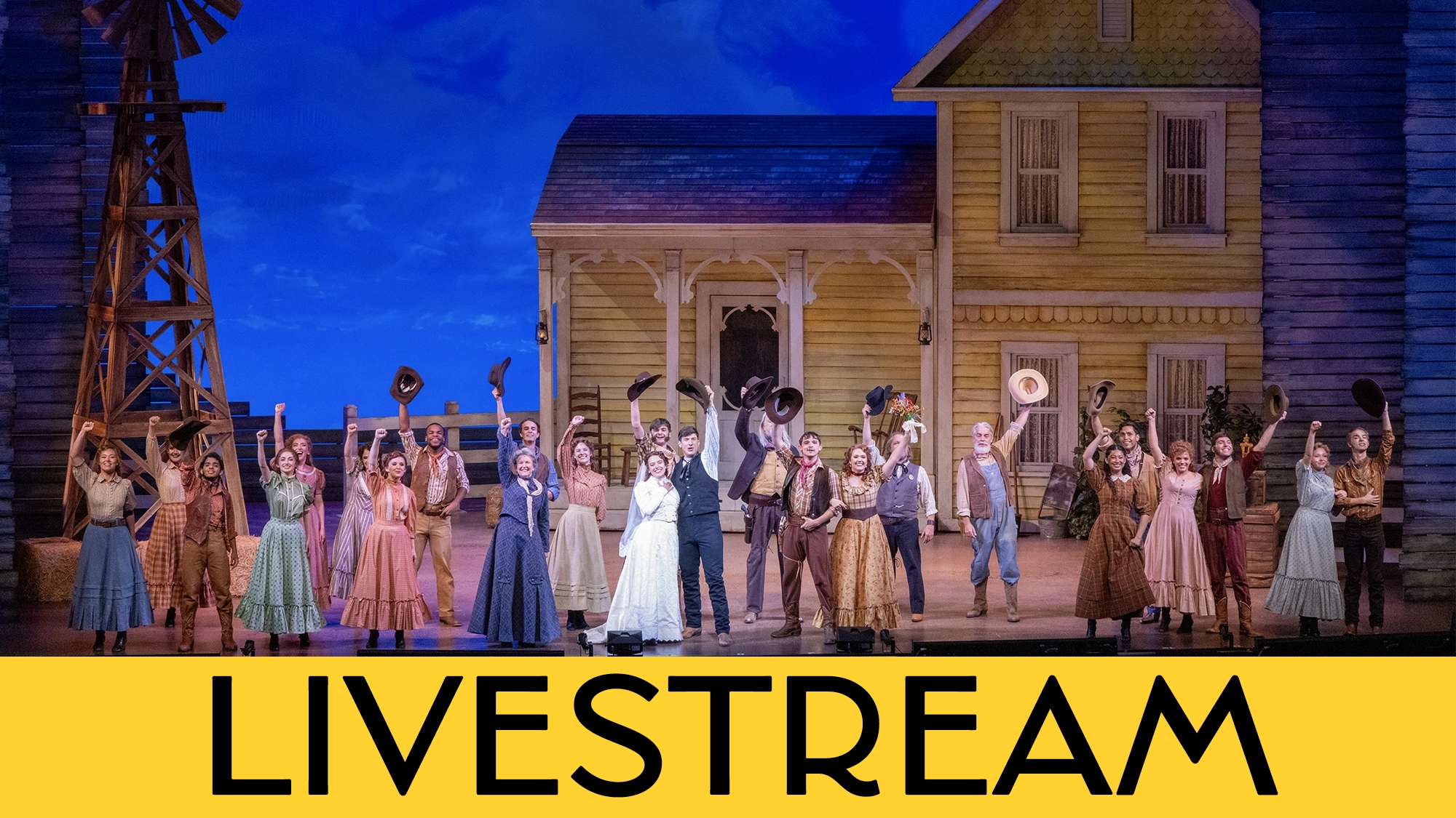 A large cast in period costumes performs onstage before a yellow farmhouse set. Many hold hats and raise their arms in celebration. The scene is lively, under blue lighting. “LIVESTREAM” in bold black letters appears across a yellow banner at the bottom.