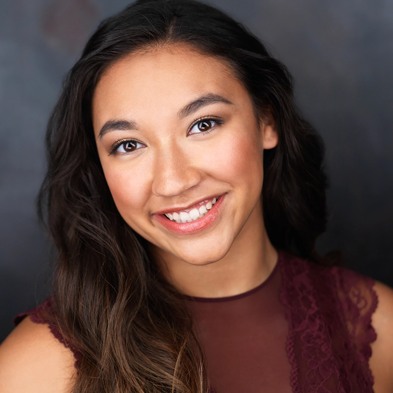 A headshot of Alexis Hasbrouck, a smiling young woman with long, dark hair wearing a maroon sleeveless top with lace detailing.