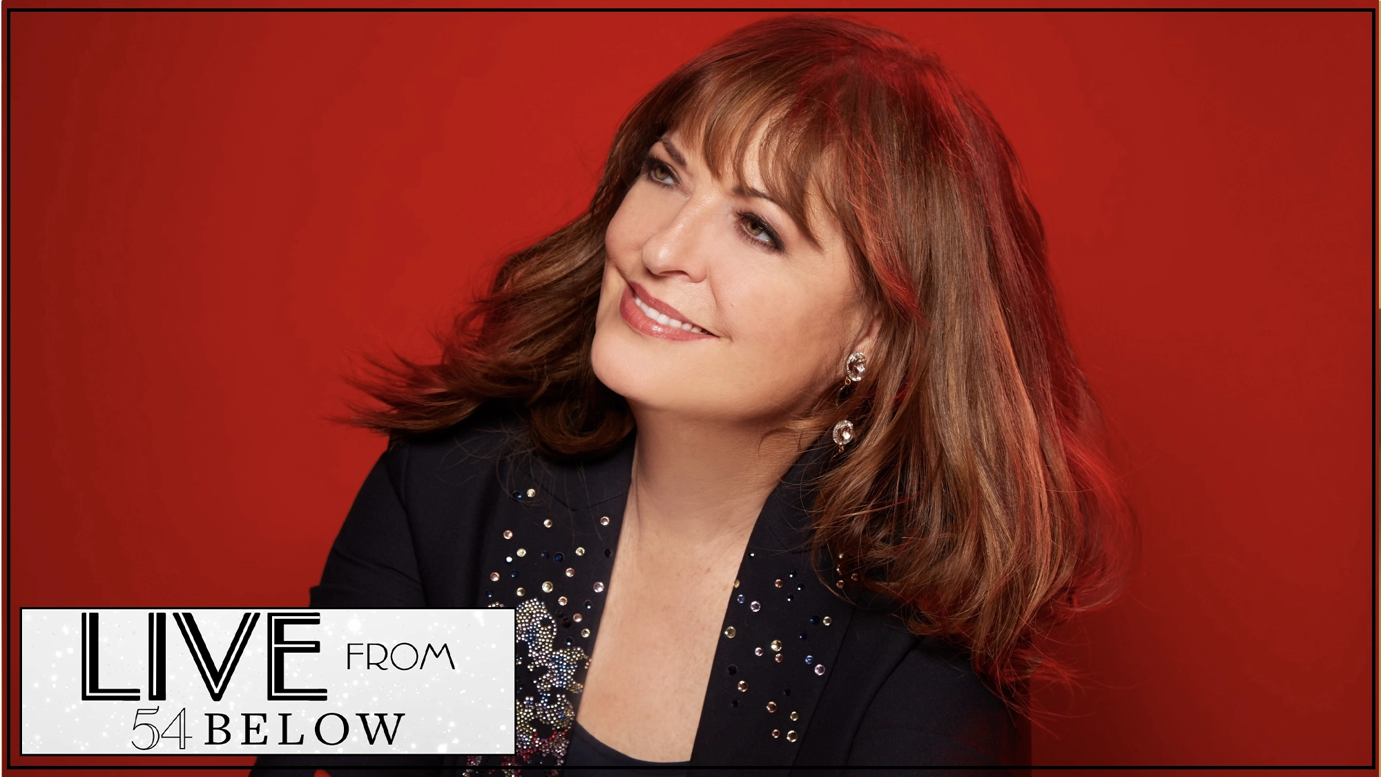 A woman with wavy brown hair and bangs smiles softly, wearing a black blazer with sparkling embellishments. Set against a vivid red background, she appears in a Livestream from 54 Below. A corner graphic reads “LIVE FROM 54 BELOW.”.
