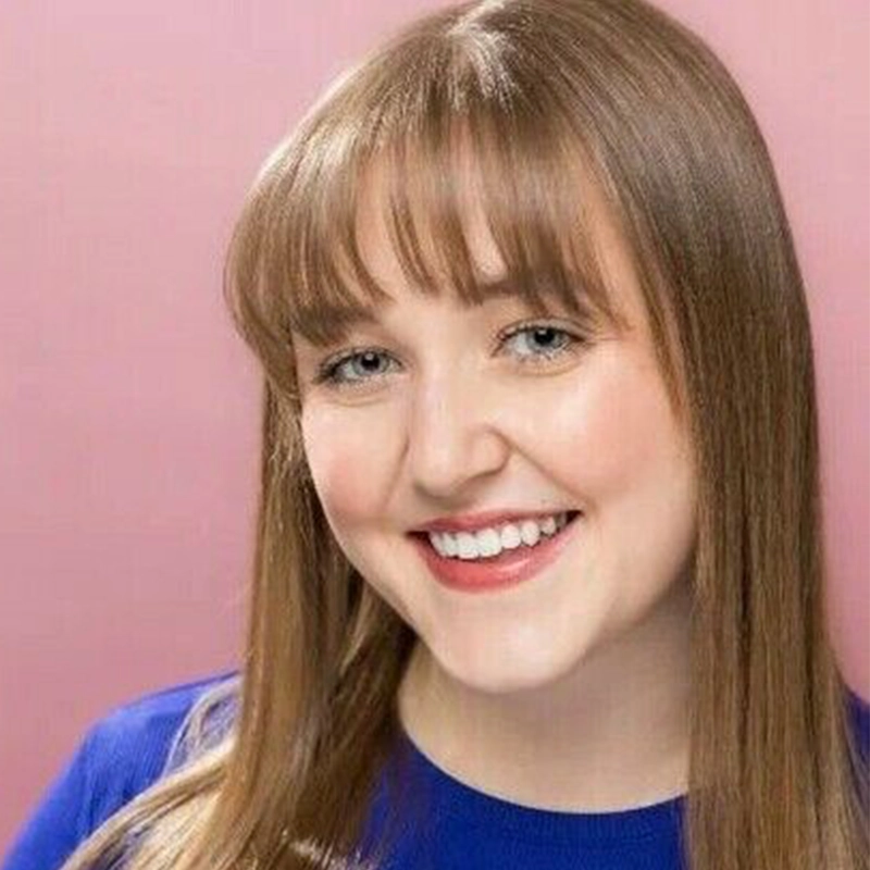 Tyler Cirulnick, a smiling young woman with long, straight brown hair and bangs, wears a blue top against a solid pink background.